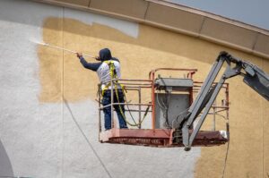 Painting Commercial business. Man Painting A Yellow wall White Using A Paint Sprayer.