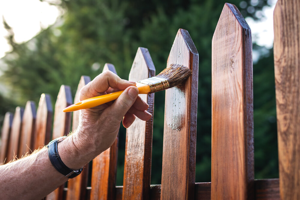 Fence Painting. Man Painting fence. Image of hand holding paint brush.