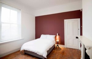 Residential painting. Accent Walls. Interior of modern bedroom with double bed and white linen, color full wall with patterns. Accent wall with maroon and blue diagonal wall paint.