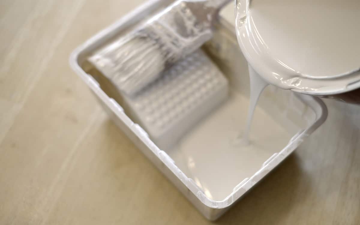 Pouring white paint into plastic paint bin with paintbrush for painting home
