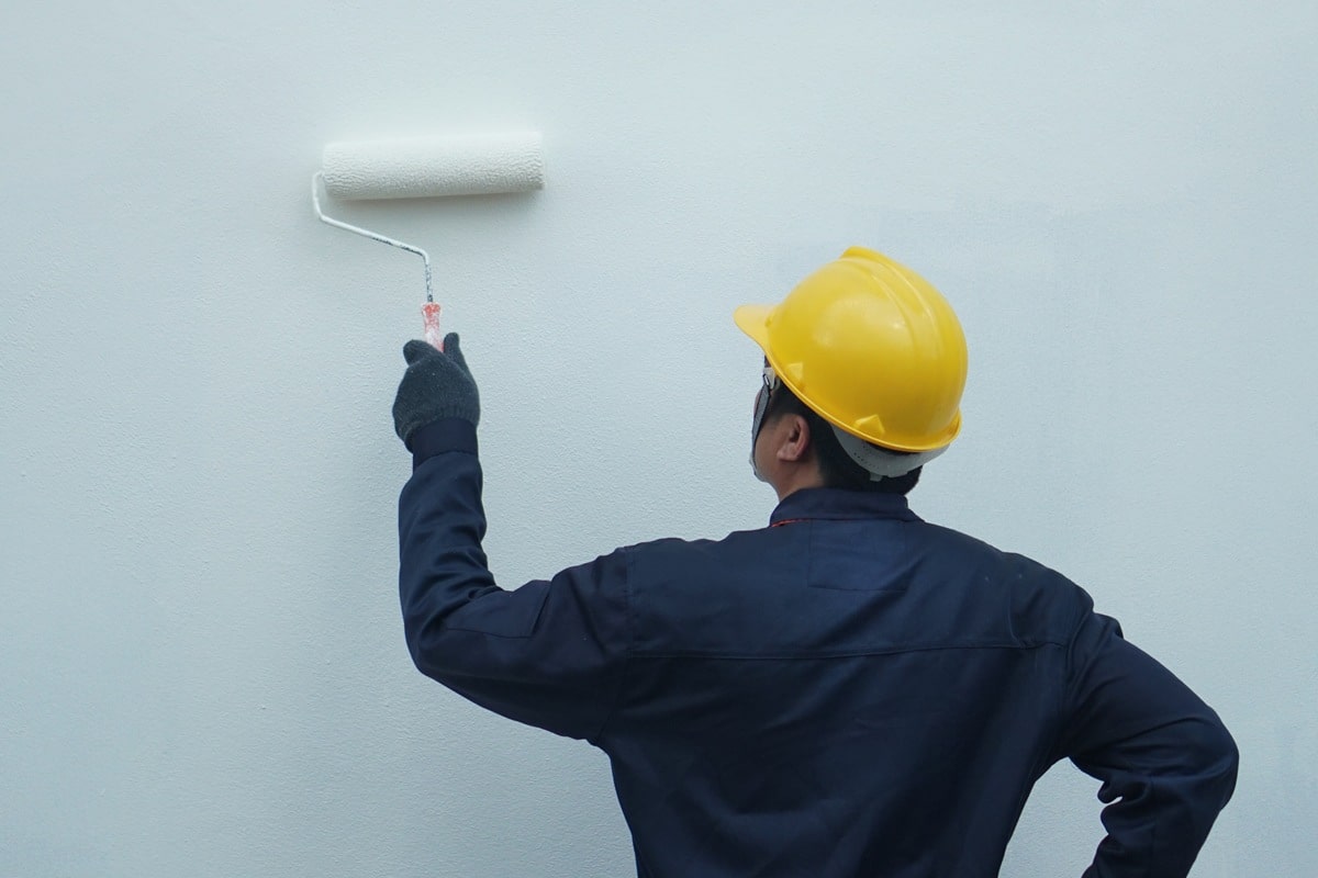 Behind the painter is painting a house wall with a roller, there is space for text.