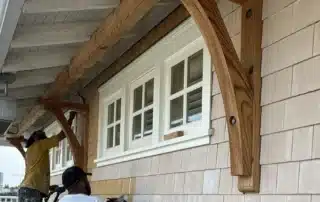 Two professional painters applying fresh white paint to shingle siding on a house exterior.